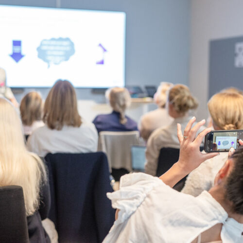 Översikt av en Wonder Women-träff tagen bakifrån rummet, kvinnor sedda bakifrån ser på en presentation.