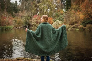 En kvinna som står vid en sjö, draperad i Stornoway-filten